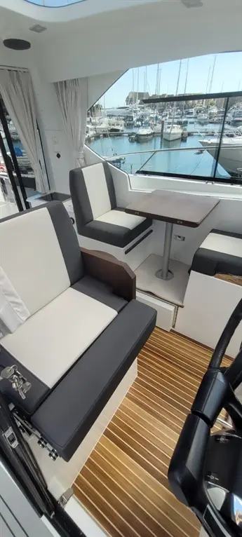 Modern yacht interior with black and white seating, a wooden table, and views of a marina filled with boats.